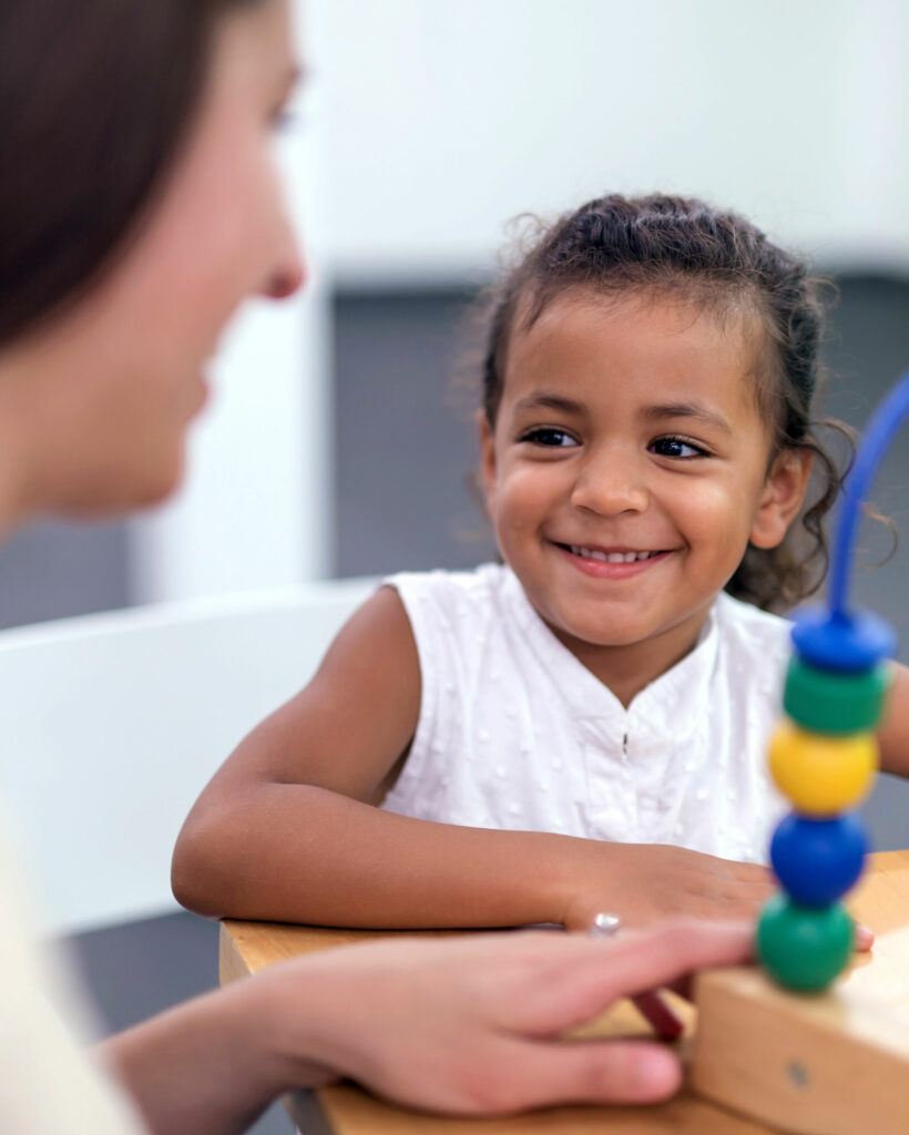 Young girl with learning toy smiling at parent or caregiver